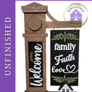 May include: A wooden DIY paint kit featuring a vertical post with the word Welcome and a hanging rectangular sign displaying the words family, Faith, and love with a heart symbol. The kit includes a small house cutout and green leaf accents.