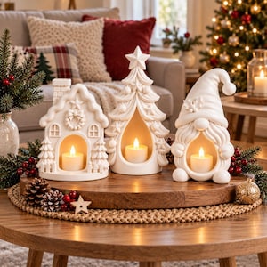 May include: Three white ceramic festive ornaments comprising a house, a Christmas tree, and a gnome, each with a hollow centre containing a lit tea light candle. The ornaments are arranged on a round wooden tray decorated with pine cones and berries.
