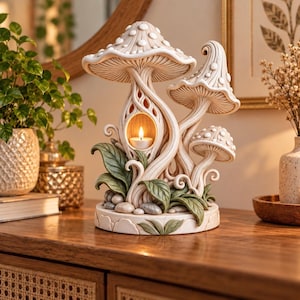 Peut inclure: Un bougeoir en forme de champignons de couleur crème avec trois chapeaux étagés, une chambre centrale creuse pour une bougie chauffe-plat, et des feuilles vertes et des pierres grises sculptées à la base en matériau mat.
