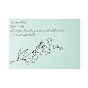 Könnte beinhalten: Eine rechteckige, hellminzgrüne Platte mit einer schwarzen Strichzeichnung eines Blumenzweigs. Der Text lautet: Be steadfast Immovable Always abounding in the work of the Lord 1 Corinthians 15:58 in einer schwarzen Schreibschrift.