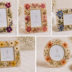 May include: A collection of five photo frames in various shapes and sizes, each featuring a clear resin border embedded with pressed dried flowers in shades of purple, pink, blue, yellow, and orange, with gold-toned metal inner edges.