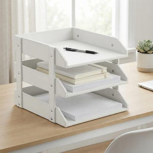 May include: A white three-tier document tray organiser with a stack of white paper and a black pen resting on the top shelf. The organiser features a sturdy frame with visible silver-toned rivets securing the side panels to the shelves.