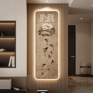 May include: A rectangular wall clock with a beige textured surface featuring a white lotus flower, several swimming fish, and a digital display showing 12:23, the date 6-2, and a temperature of 26 degrees. The clock is illuminated by a soft back light.