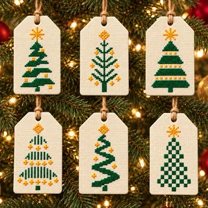 Può includere: Sei etichette rettangolari in tessuto color crema con disegni di alberi di Natale ricamati a punto croce in verde e giallo. Ogni etichetta è dotata di un cordino in juta per appenderla e presenta un motivo geometrico unico con una stella.