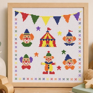Puede incluir: Un bordado en punto de cruz enmarcado con un tema de circo colorido sobre tela blanca. El diseño incluye una carpa de circo central, cinco figuras de payasos y una guirnalda festiva en la parte superior, todo bordeado por un patrón multicolor.