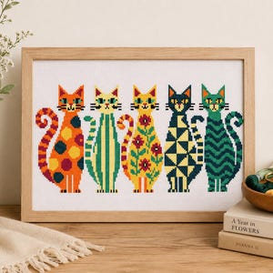Könnte beinhalten: Ein gerahmtes Kreuzstich-Stickbild mit fünf stilisierten Katzen in einer Reihe. Jede Katze zeigt ein einzigartiges Muster: orange mit Punkten, grün mit vertikalen Streifen, gelb mit Blumenmotiven, dunkelblau mit geometrischen Formen und blaugrün mit Wellen.