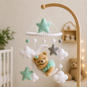 Può includere: Una giostrina per culla all'uncinetto con una luna crescente bianca centrale e un orsetto marrone chiaro che dorme con un tutù verde menta. La giostrina include stelle verde menta e grigie, nuvole bianche e piccole sfere bianche sospese.