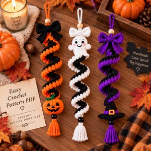 May include: Three hanging crochet spiral ornaments. The left features an orange and black spiral with a pumpkin and black bow. The center is a white and black spiral with a ghost and white bow. The right is a purple and black spiral with a witch hat and purple bow.