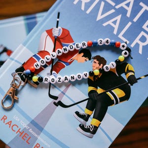 May include: A beaded keyring featuring two strands of colourful plastic beads with white letter beads spelling out HOLLANDER 24 and ROZANOV 81, accented with small star and heart beads, finished with a silver-toned metal lobster clasp attachment.