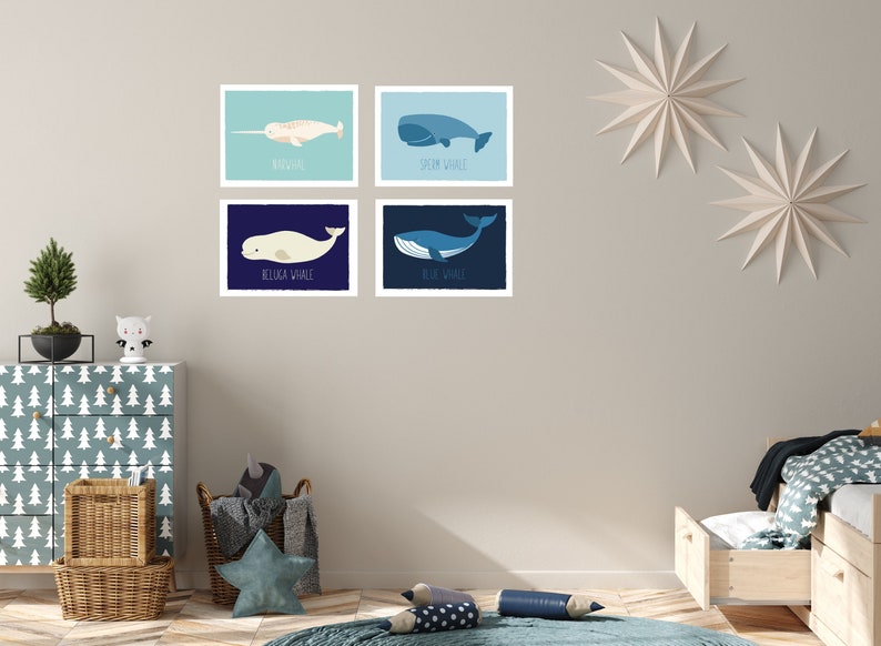 May include: Four framed whale illustrations. The top left features a narwhal, the top right a sperm whale, the bottom left a beluga whale, and the bottom right a blue whale. Each illustration has the whale's name below it. The artwork is displayed in a child's room.
