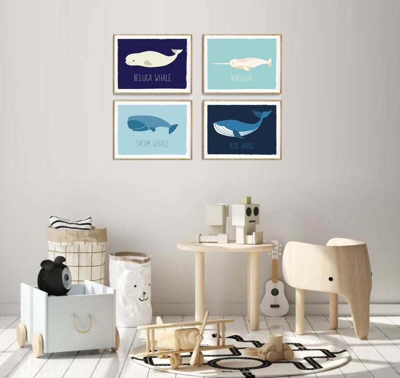 May include: Four framed art prints featuring illustrations of whales: Beluga Whale, Narwhal, Sperm Whale, and Blue Whale. Each print has a different background color and the whale's name is printed below the illustration. The prints are displayed in a child's room.