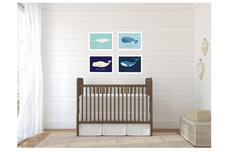 May include: Four framed whale art prints in a nursery setting. The prints feature illustrations of different whales, including a narwhal and a blue whale, in shades of blue and white. A wooden crib and neutral decor complete the scene.
