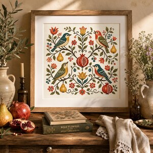 Peut inclure: Une broderie au point de croix encadrée de forme carrée présentant un motif botanique symétrique avec quatre oiseaux, deux grenades et deux poires. Le motif inclut des fleurs rouges, jaunes et bleues sur un fond crème, le tout dans un cadre en bois clair.