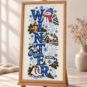 May include: A framed cross-stitch embroidery piece featuring the word WINTER in large blue letters. The design includes a snowman, a lantern, a snow-covered cabin, blue mittens, a mug of hot cocoa, and white ice skates, all accented with snowflakes.