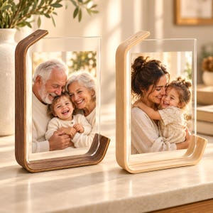 May include: Two vertical photo frames with clear acrylic panels and curved wooden bases. The left frame features a dark walnut wood base holding a photo of an elderly couple and a child. The right frame has a light oak wood base with a photo of an adult and a child.
