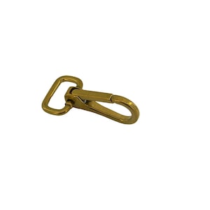 May include: A brass-toned metal swivel lobster clasp featuring a rectangular loop at one end and a spring-loaded gate mechanism. The hardware has a smooth, polished finish and a curved, elongated hook design for secure attachment.