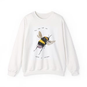 May include: A white long-sleeve sweatshirt featuring a watercolor-style illustration of a bumblebee in the center. The text "You can call me" is printed above the bee, and "honey if you want" is printed below the bee in black font.