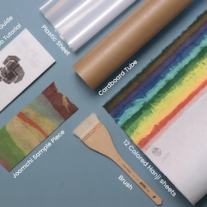 May include: A Joomchi collage kit containing an illustrated guide with QR video tutorial, a plastic sheet, a brown cardboard tube, a Joomchi sample piece, a wooden brush, and 12 colored Hanji sheets arranged in a rainbow gradient pattern.