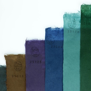 May include: A series of vertical strips of textured paper arranged in a stepped pattern, featuring colors including dark gray, brown, purple, blue, teal, dark green, and light green. Each strip displays a circular stamp and a unique number.