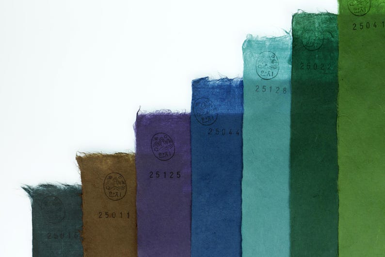 May include: A series of vertical strips of textured paper arranged in a stepped pattern, featuring colors including dark gray, brown, purple, blue, teal, dark green, and light green. Each strip displays a circular stamp and a unique number.
