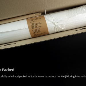 May include: A white, textured roll of Hanji paper secured with white string, wrapped in a brown paper label with printed text, and placed inside a rectangular cardboard shipping box for protection during transit.