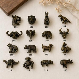 May include: A collection of sixteen antique brass-toned metal animal-shaped knobs, each labeled with a three-digit number from 101 to 116. The figures include a horse, lion, rabbit, dinosaur, buffalo, elephant, bull, monkey, bear, dog, and rhinoceros.