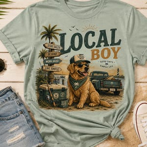May include: A sage green t-shirt featuring a graphic of a golden retriever wearing a cap and sunglasses, a bandana, a cooler, a signpost with the text STAY SALTY, BE KIND, WORK HARD, LIVE SIMPLE, a pickup truck, and the text LOCAL BOY GOOD DAYS SIMPLE LIFE.