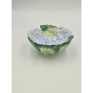 May include: A ceramic bowl featuring a sculpted design of light blue hydrangea flowers and green leaves. The exterior and interior surfaces are textured to mimic the appearance of natural foliage, with a glossy finish and detailed petal relief.