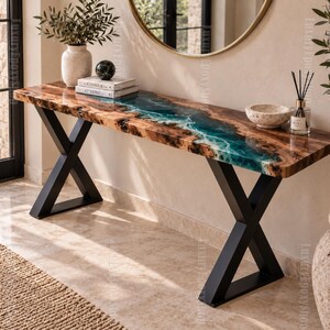 Pode incluir: Uma mesa consola retangular com um tampo de madeira natural de borda irregular e uma incrustação central de resina epóxi translúcida em tons de azul-petróleo e branco. A mesa é suportada por duas pernas de metal preto em forma de X.