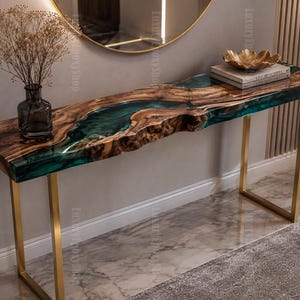 Op de afbeelding: Een rechthoekige sidetable met een natuurlijk houten blad met boomrand en een centrale inleg van doorschijnende smaragdgroene hars. De tafel rust op twee U-vormige poten van geborsteld goudkleurig metaal en bevat een glazen vaas.