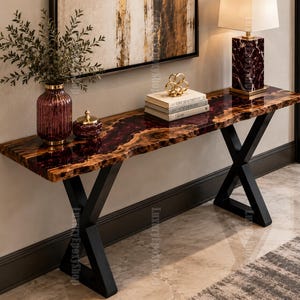 May include: A console table featuring a live edge wood slab surface with a deep red epoxy resin inlay, supported by black metal X-shaped legs. The table holds a purple glass vase, a small lidded jar, a stack of books, a gold sculpture, and a lamp.