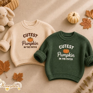 May include: Two long-sleeve ribbed knit sweaters, one cream and one dark green, each featuring the embroidered text "CUTEST Pumpkin IN THE PATCH" with a small orange pumpkin graphic centered on the chest, designed with a crew neckline.