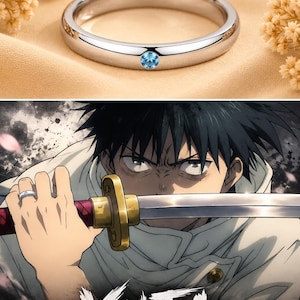 May include: A polished silver-tone band ring featuring a single, small, round, light blue gemstone set flush into the metal. The ring is displayed alongside an anime-style illustration of a character holding a sword with the text YUTA JJK.