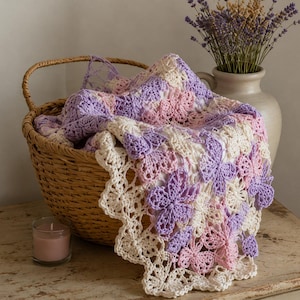 May include: A handmade crochet blanket featuring a repeating butterfly motif in shades of lavender, soft pink, and cream. The blanket is draped over a woven wicker basket, showcasing an intricate openwork border and delicate yarn construction.