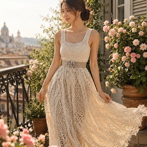 May include: A cream-colored sleeveless crochet maxi dress featuring a square neckline and an intricate openwork knit pattern. The dress is cinched at the waist with a wide, light beige belt that has a decorative silver-toned metal buckle.