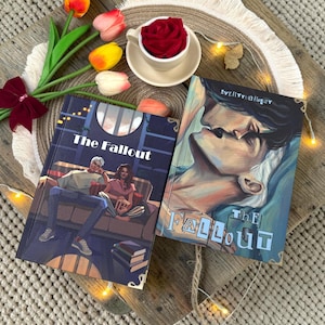 May include: Two hardcover books titled The Fallout with illustrated covers, one showing a couple on a couch and the other a close-up of two faces, accompanied by a white teacup containing a red rose and several colorful tulip stems.