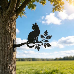 Peut inclure: Une silhouette en métal noir représentant un chat assis sur une branche d'arbre, fixée au tronc. Le chat est représenté de profil, tourné vers la gauche, avec la queue recourbée vers le bas. La branche présente plusieurs feuilles détaillées.