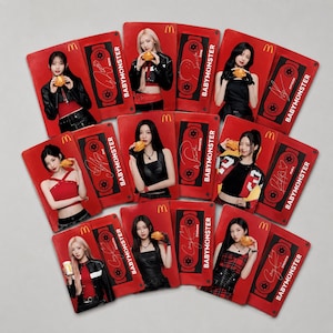 Puede incluir: Una colección de tarjetas coleccionables rectangulares con miembros del grupo BABYMONSTER. Cada tarjeta muestra un retrato de un miembro sosteniendo una hamburguesa, el logotipo de McDonald's, un gráfico de casete, una firma y el texto BABYMONSTER.