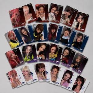Puede incluir: Una colección de tarjetas fotográficas rectangulares con retratos de varias personas con diversos colores y estilos de cabello. Cada tarjeta muestra el texto DM 2ND MINI ALBUM en la parte inferior. Las tarjetas están dispuestas de forma dispersa sobre un fondo liso.