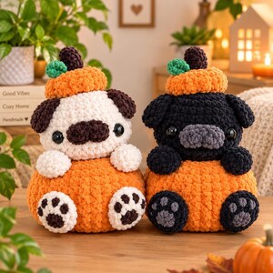May include: Two crocheted plush toys shaped like pugs sitting inside orange pumpkins. One pug is white with dark brown ears and a dark brown snout, while the other is black with a grey snout. Both have black eyes and a small green leaf on top.