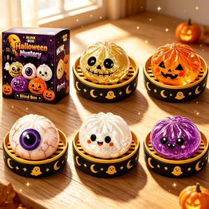 May include: A Blink Box Halloween Mystery blind box set featuring five small, round, squishy figures shaped like dumplings, each resting on a black and yellow steamer basket base decorated with ghost and moon icons, including an eyeball and pumpkin designs.