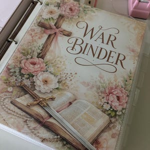 May include: A binder with the words "War Binder" in elegant script, adorned with floral illustrations and a wooden cross. An open book and a sword are also visible.