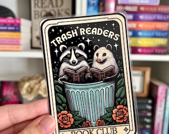 May include: A rectangular sticker featuring a raccoon and an opossum reading books inside a light blue trash can. The design includes orange roses, green leaves, and the text "TRASH READERS" at the top and "BOOK CLUB" at the bottom, all enclosed in a cream-coloured border.