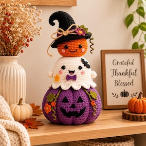 Peut inclure: Une décoration en crochet empilée composée d'une citrouille violette à la base, d'un fantôme blanc avec un nœud papillon violet au milieu, et d'une citrouille orange portant un chapeau de sorcière noir avec une fleur et un nœud en ficelle.