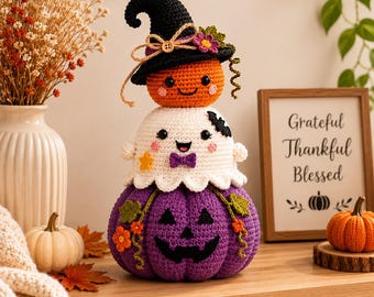 May include: A stacked crochet decoration featuring a purple jack-o'-lantern base, a white ghost with a purple bow tie in the middle, and an orange pumpkin wearing a black witch hat with a small flower and twine bow on top.