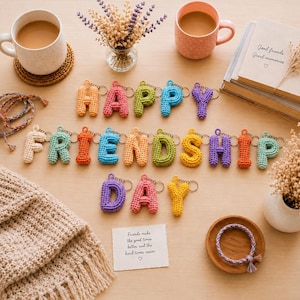 May include: A collection of colorful, crocheted letter keychains spelling out HAPPY FRIENDSHIP DAY. Each individual letter is crafted from yarn in various bright hues, including orange, pink, green, blue, yellow, and cream, and features a metal ring.