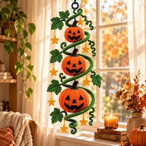 May include: A vertical hanging decoration featuring three crocheted orange jack-o'-lanterns with dark brown stems, connected by a spiralling green vine. The vine is adorned with crocheted green leaves and small yellow stars hanging from thin threads.
