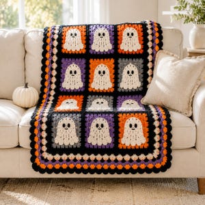 May include: A handmade crochet blanket featuring a grid of square panels, each displaying a white ghost with black eyes and a mouth. The squares are bordered by orange, purple, and gray yarn, with a black scalloped edge framing the entire piece.