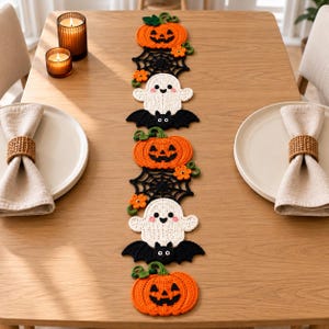 Puede incluir: Un camino de mesa decorativo de ganchillo largo con un patrón de Halloween repetitivo. El diseño incluye calabazas naranjas, telarañas negras, fantasmas blancos con mejillas rosadas y murciélagos negros, acentuados con pequeñas flores naranjas y hojas.