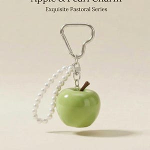 May include: A keychain featuring a glossy light green apple charm with a brown stem, attached to a silver-toned metal carabiner and a loop of small white faux pearls. The text Handcrafted Green Apple & Pearl Charm Exquisite Pastoral Series is visible.